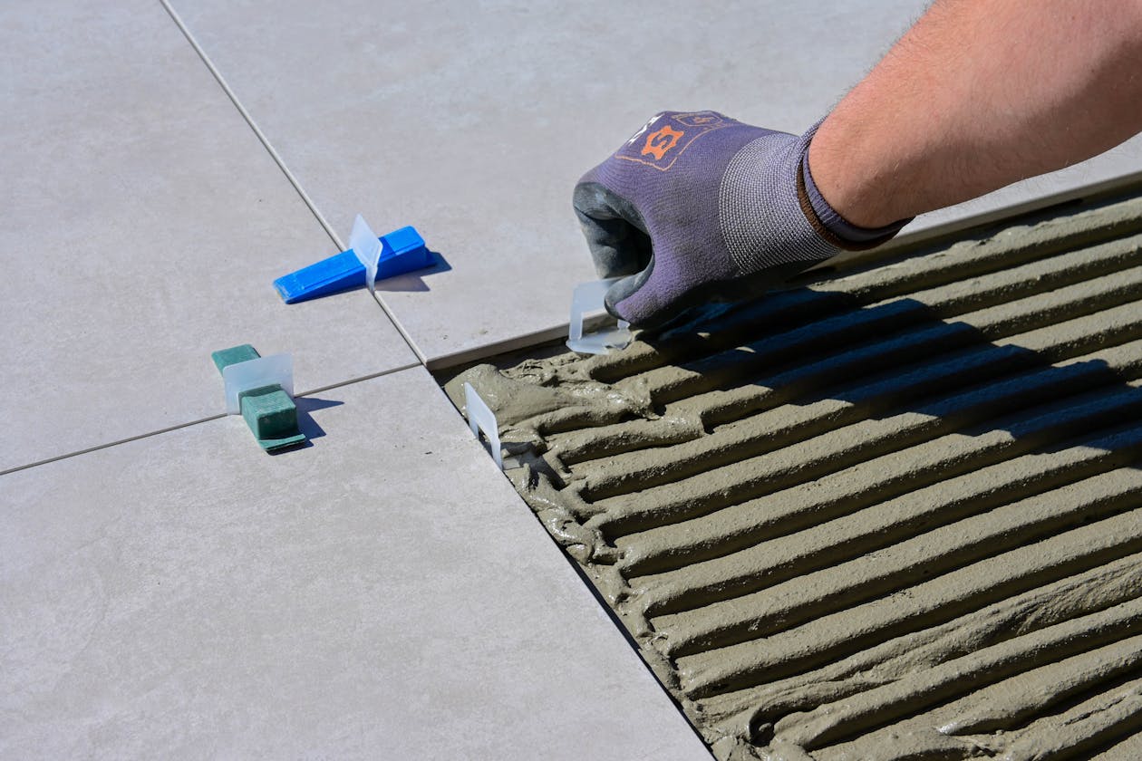 Detailed view of gloved hand aligning tiles with levelers and spacers during construction. — epoxy flooring company omaha