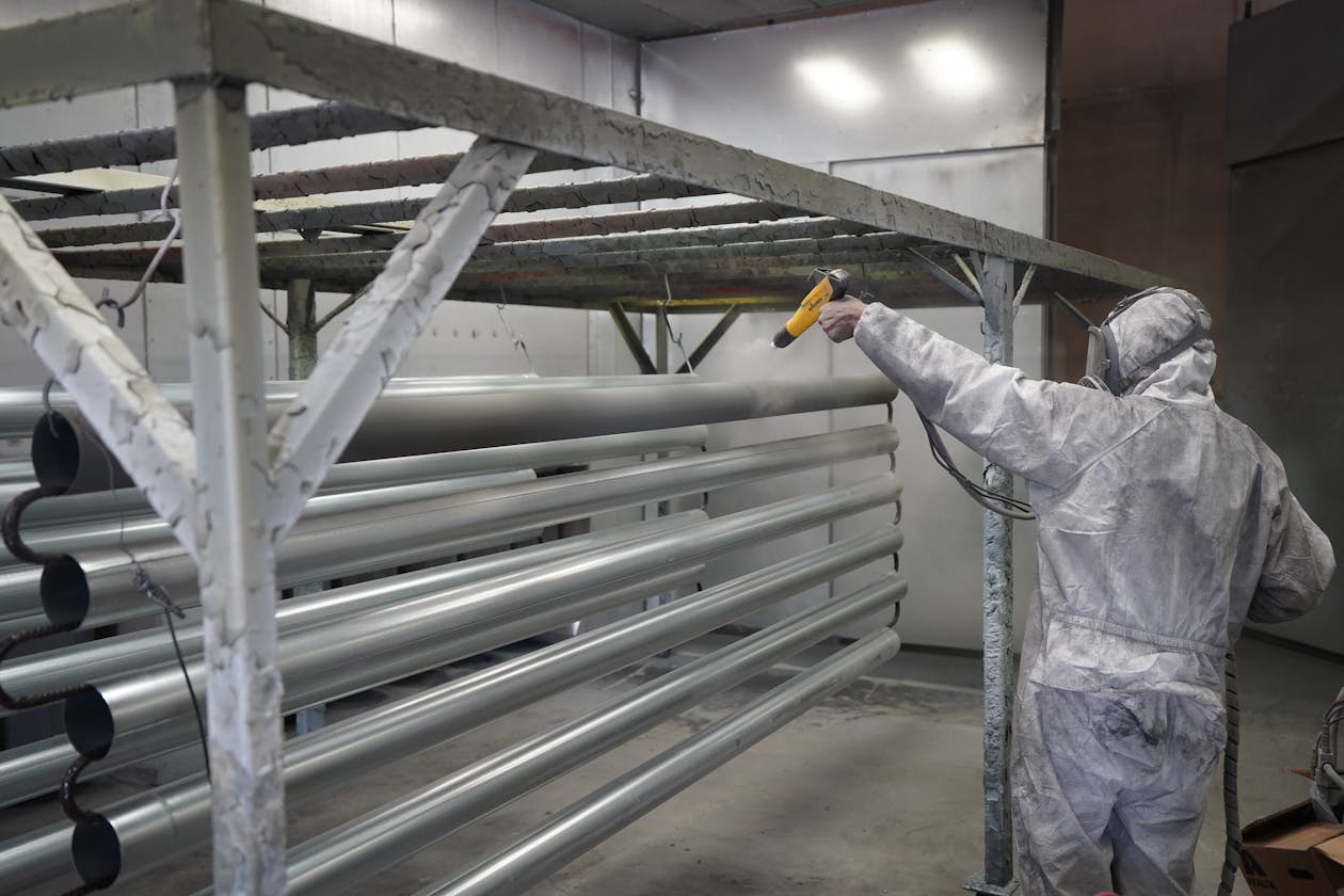 Technician applying powder coating to metal pipes in a workshop setting. — driveway epoxy coating