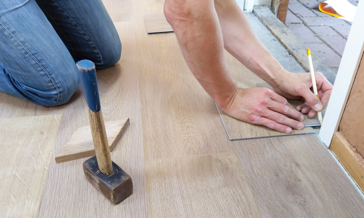A craftsman carefully measures and marks wooden floor panels for precise installation. — automotive dealership floor coating